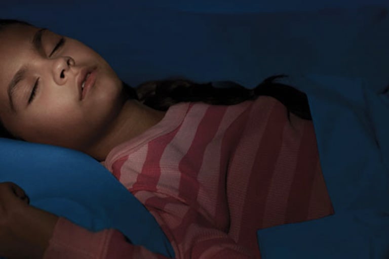 Una niña con una camisa roja a rayas durmiendo profundamente en su cama.