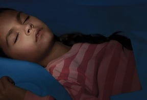 Una niña con una camisa roja a rayas durmiendo profundamente en su cama.