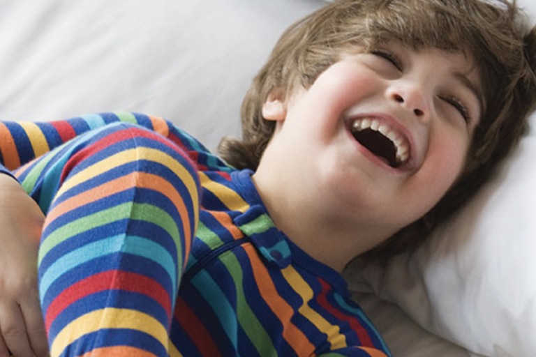 A Young boy laughing  while resting on bed