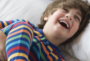 A Young boy laughing  while resting on bed