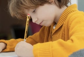 Boy sitting at place writing with a pencil